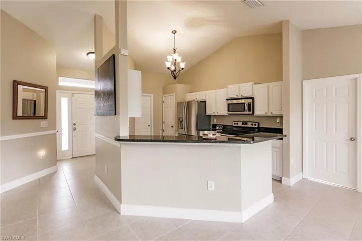 Kitchen with appliances with stainless steel finishes, vaulted ceiling, kitchen peninsula, hanging light fixtures, and light tile patterned flooring