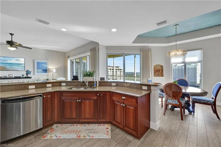 Kitchen with stainless steel dishwasher, light stone countertops, pendant lighting, wood tiled floors, and a raised ceiling