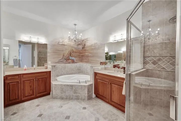 Bathroom featuring suspended lighting, two vanities, a shower stall, and a garden tub