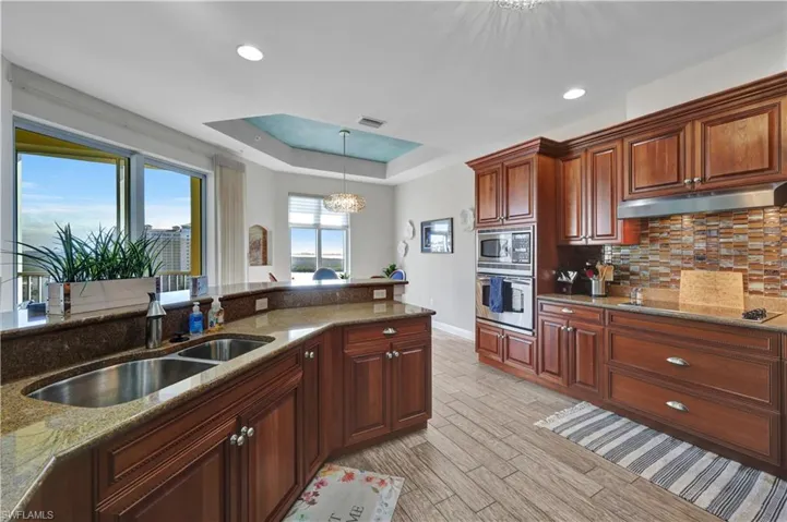 Kitchen with light stone counters, stainless steel appliances, hanging lights, and a raised ceiling