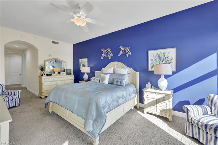 Bedroom featuring arched walkways, carpet floors, a ceiling fan, and an accent wall