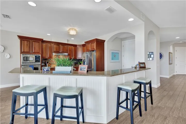 Kitchen featuring a kitchen breakfast bar, light wood-type flooring, light stone countertops, stainless steel appliances, and recessed lighting