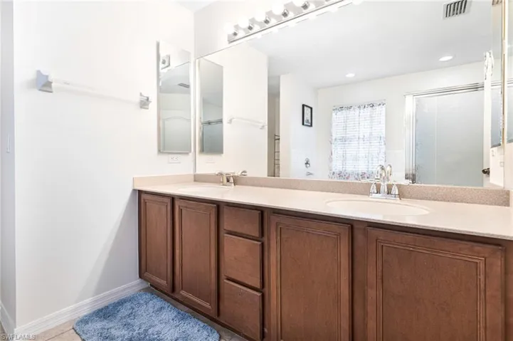 Bathroom featuring double vanity, visible vents, a sink, and a shower with shower door