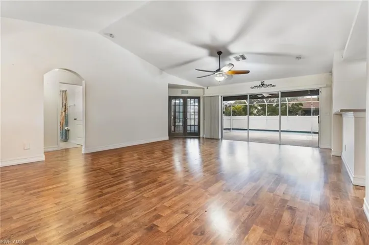 Empty room with a ceiling fan, visible vents, arched walkways, vaulted ceiling, and wood finished floors