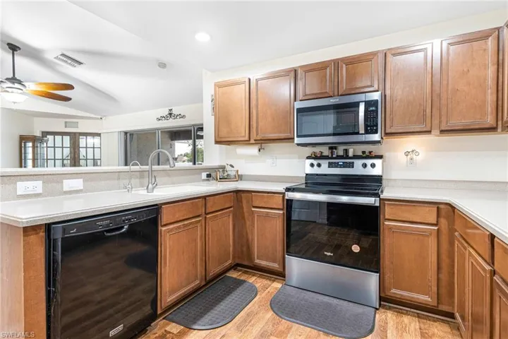 Kitchen featuring a sink, a peninsula, light wood-style floors, a ceiling fan, and appliances with stainless steel finishes