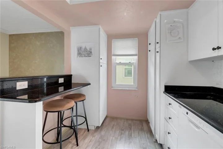 Kitchen with light wood-style flooring, white dishwasher, white cabinetry, a kitchen bar, and crown molding