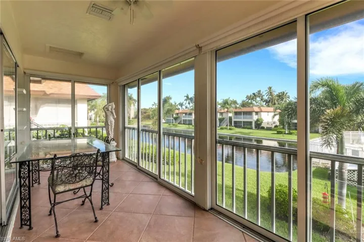 Sunroom featuring a water view, tile patterned flooring, a ceiling fan, and a residential view