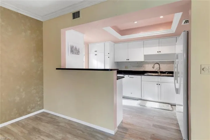 Kitchen with white appliances, light wood-type flooring, white cabinetry, tasteful backsplash, and dark countertops
