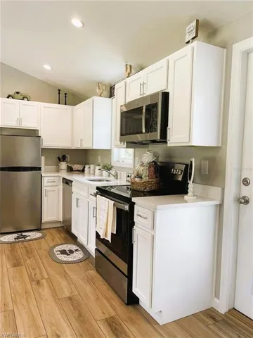 Kitchen featuring sink, light hardwood / wood-style flooring, white cabinetry, appliances with stainless steel finishes, and vaulted ceiling