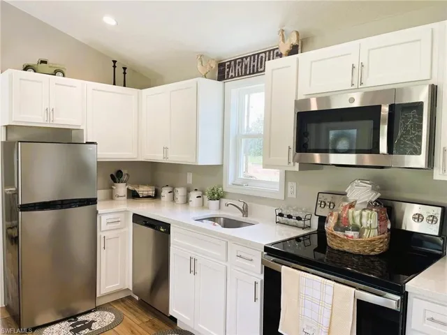 Kitchen with sink, vaulted ceiling, white cabinetry, light hardwood / wood-style flooring, and stainless steel appliances