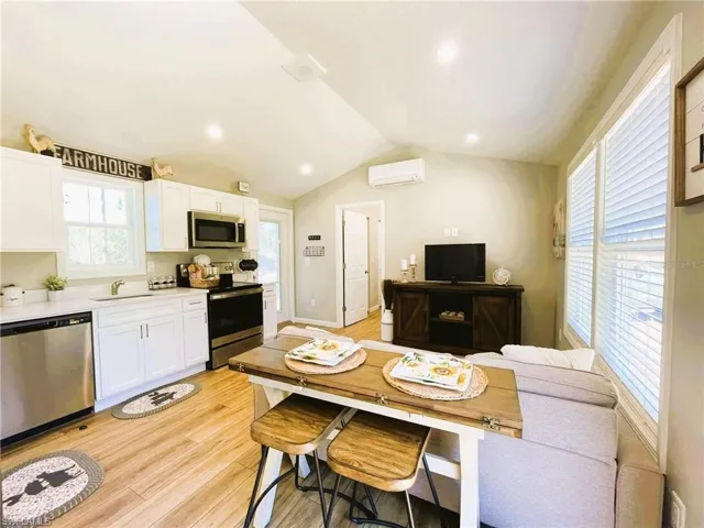 Kitchen with an AC wall unit, white cabinets, lofted ceiling, light hardwood / wood-style flooring, and appliances with stainless steel finishes
