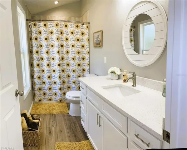 Bathroom featuring toilet, hardwood / wood-style flooring, lofted ceiling, vanity, and curtained shower