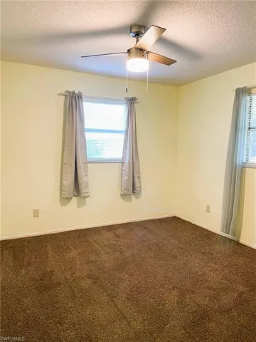 Empty room featuring dark colored carpet, a textured ceiling, and a ceiling fan