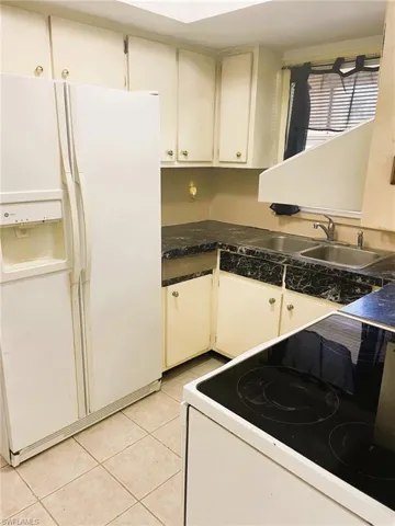 Kitchen featuring white appliances, white cabinetry, light tile patterned flooring, and tile counters
