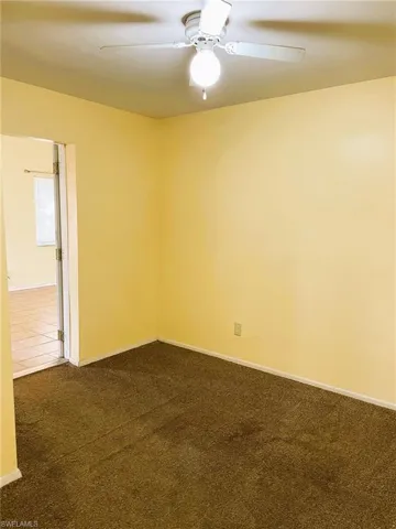 Unfurnished room with dark colored carpet and ceiling fan