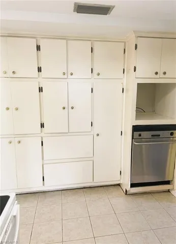 Kitchen with stainless steel dishwasher, white range, light tile patterned floors, and white cabinets