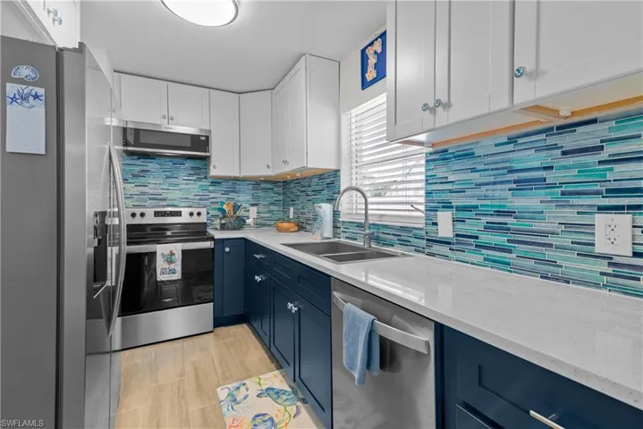 Kitchen featuring decorative backsplash, appliances with stainless steel finishes, light stone countertops, sink, and white cabinetry