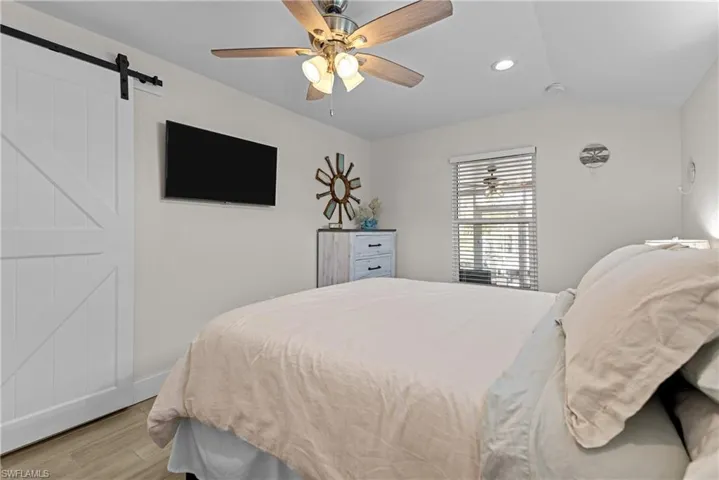 Bedroom featuring a barn door, light hardwood / wood-style floors, vaulted ceiling, and ceiling fan