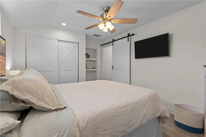 Bedroom featuring lofted ceiling, ceiling fan, a barn door, light hardwood / wood-style floors, and a closet
