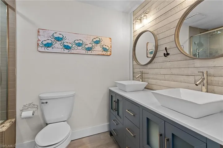 Bathroom with walk in shower, vanity, wooden walls, hardwood / wood-style floors, and toilet