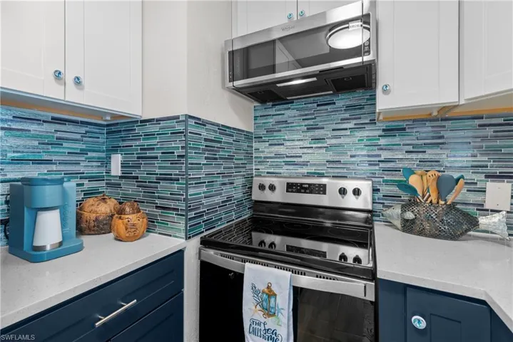 Kitchen featuring decorative backsplash, blue cabinets, white cabinets, and appliances with stainless steel finishes