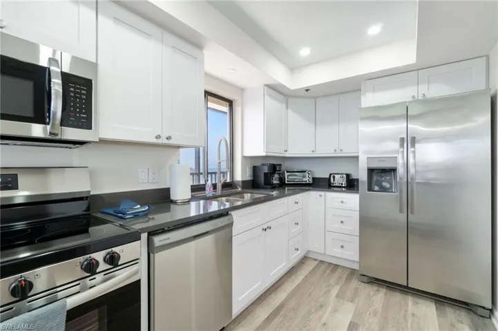 Kitchen with appliances with stainless steel finishes, white cabinetry, light wood finished floors, recessed lighting, and dark stone countertops