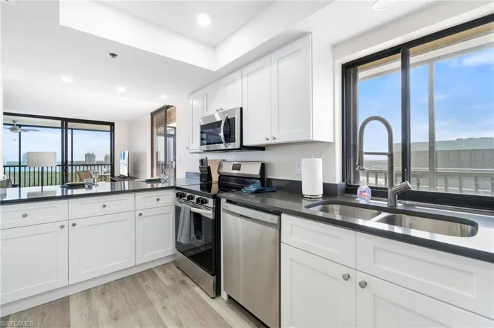 Kitchen with white cabinets, stainless steel appliances, light wood finished floors, recessed lighting, and dark stone countertops