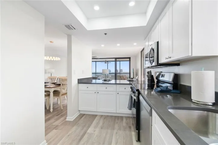 Kitchen with light wood-style flooring, stainless steel appliances, white cabinetry, a tray ceiling, and recessed lighting
