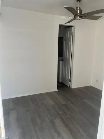 Unfurnished room featuring dark wood-type flooring, baseboards, and ceiling fan