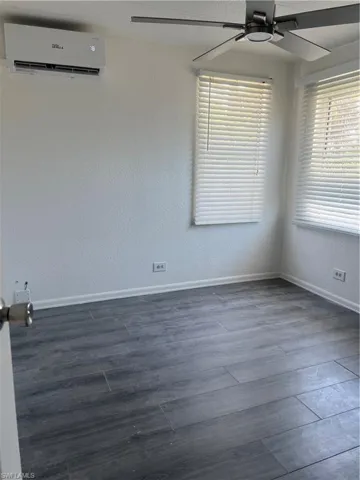 Empty room featuring baseboards, a ceiling fan, a wall unit AC, and dark wood-style flooring