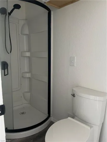 Bathroom featuring wood finished floors, a shower stall, and toilet