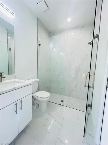 Bathroom with vanity, a marble finish shower, light marble finish flooring, and recessed lighting