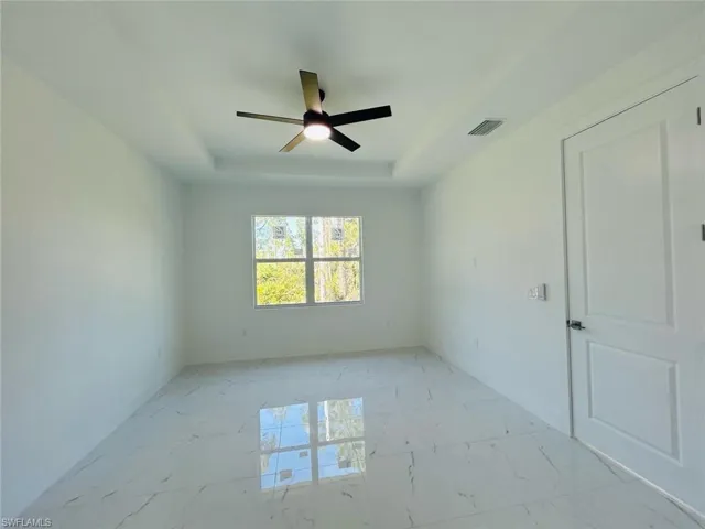 Spare room featuring a raised ceiling, light marble finish flooring, and a ceiling fan