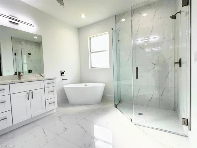 Full bath with vanity, a marble finish shower, light marble finish floors, a soaking tub, and recessed lighting