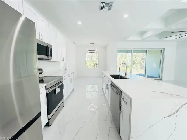 Kitchen with appliances with stainless steel finishes, recessed lighting, white cabinetry, light stone counters, and coffered ceiling