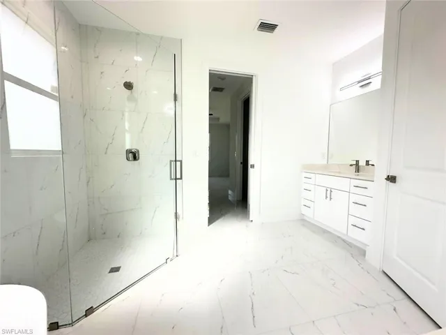 Full bath featuring vanity, a marble finish shower, and light marble finish flooring