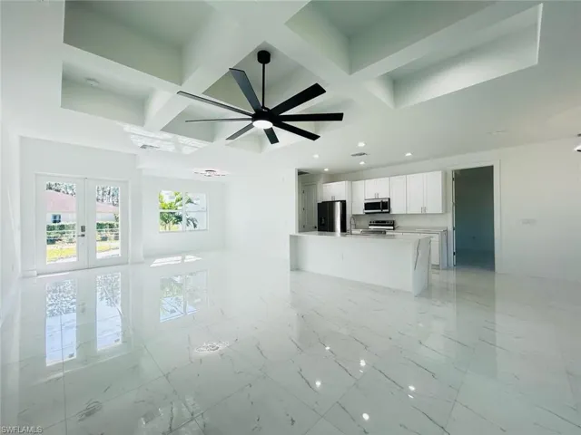 Unfurnished living room featuring french doors, coffered ceiling, beamed ceiling, light marble finish flooring, and a ceiling fan