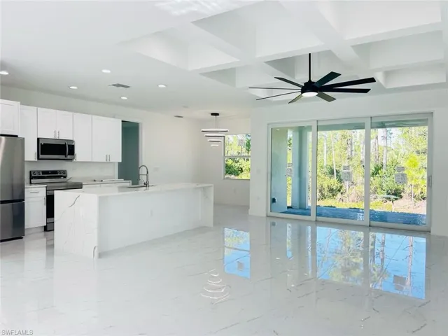 Kitchen featuring appliances with stainless steel finishes, coffered ceiling, light stone countertops, light marble finish flooring, and a kitchen island with sink