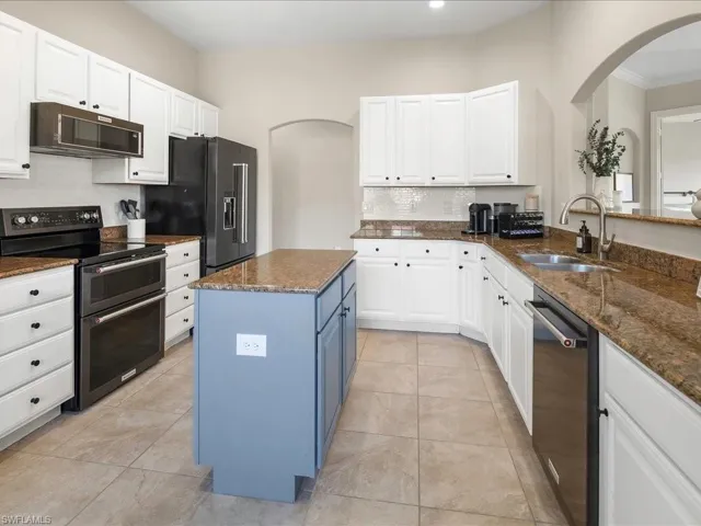Kitchen featuring arched walkways, black appliances, blue cabinets, white cabinets, and dark stone counters