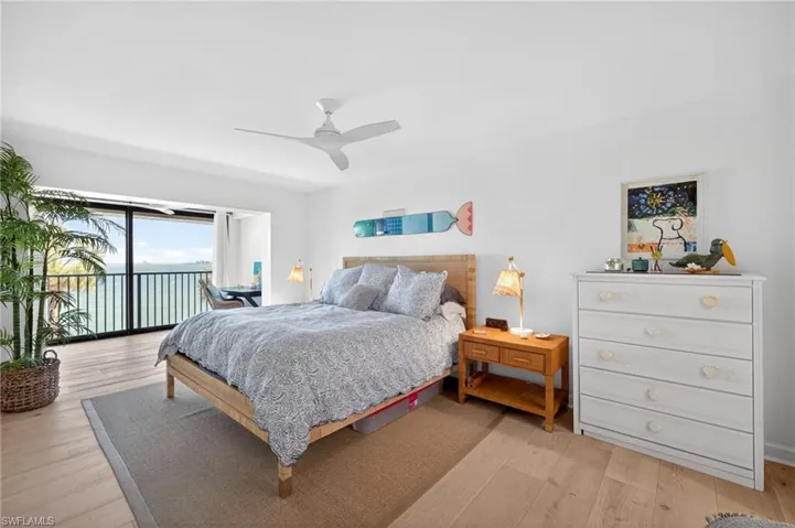 Primary Bedroom featuring light wood-finish flooring, a contemporary ceiling fan, and sliding glass doors opening to a balcony with water scenery