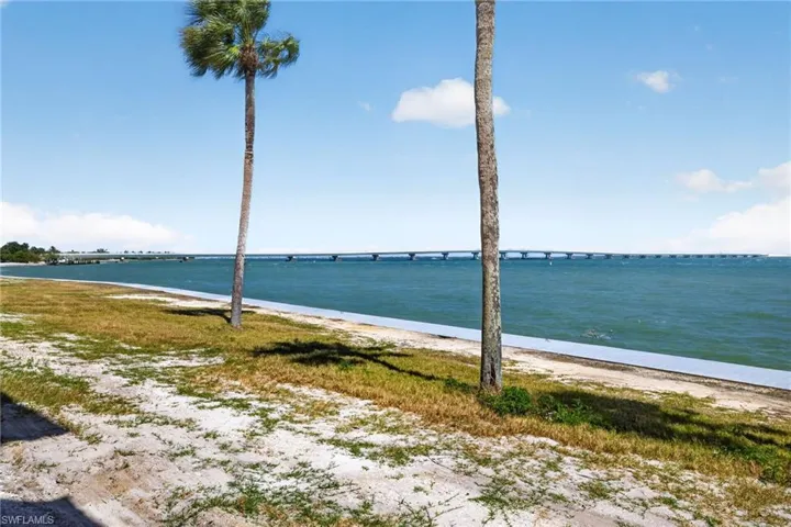 Waterfront property featuring a bridge spanning the water, a sandy and grassy shoreline, and palm trees