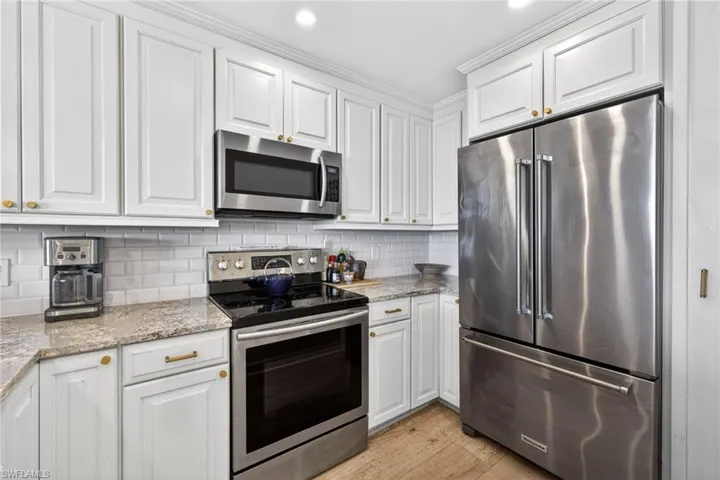Kitchen featuring white cabinetry with gold-toned hardware, stainless steel appliances, speckled countertops, and a white subway tile backsplash