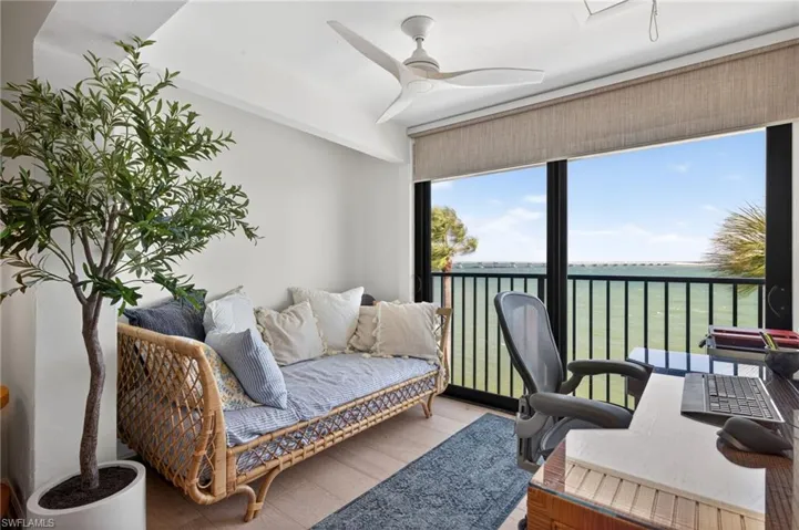 Expansive window overlooking a body of water with a distant bridge, featuring a ceiling fan, light-toned wood-finish flooring, and a textured roller shade