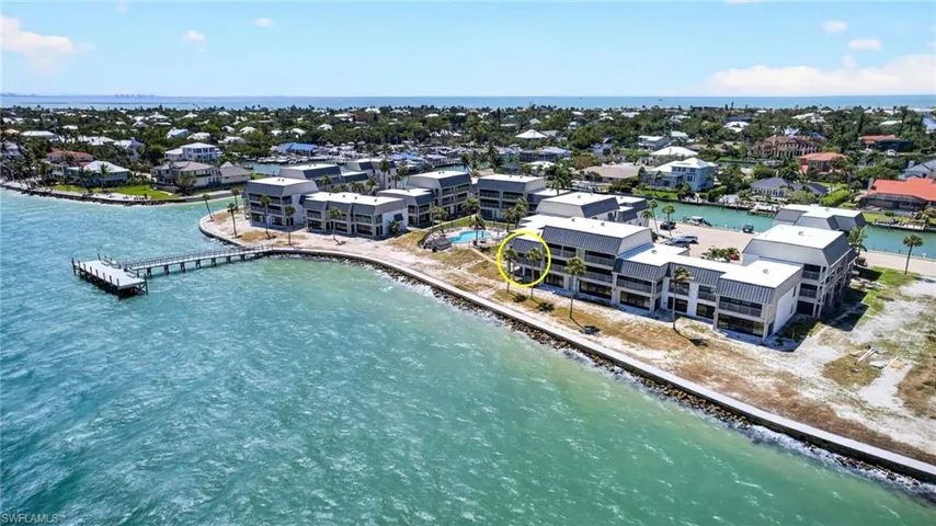 Waterfront condominium complex featuring multiple buildings with private balconies, a dock extending into the water, and an outdoor swimming pool