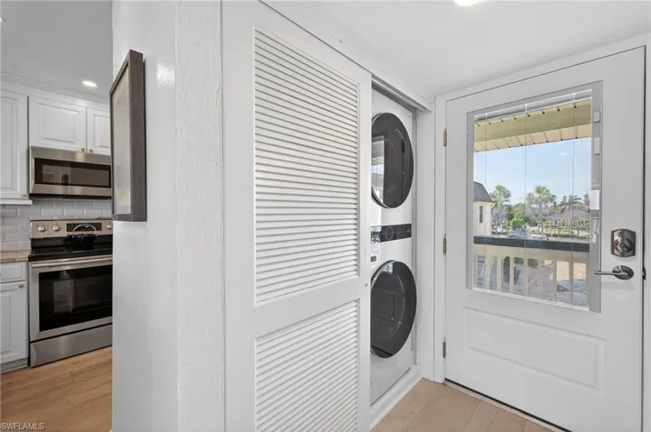Stacked laundry appliances within a louvered closet, complemented by a white paneled door with an integrated window