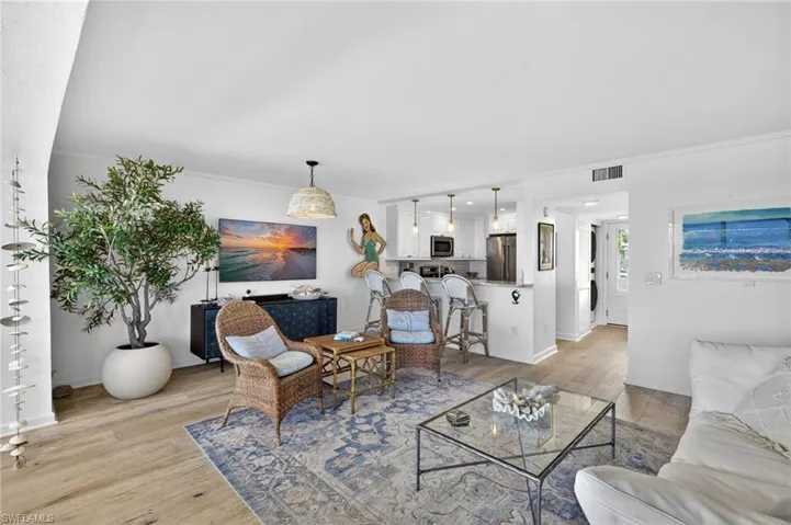 Open-concept living space with wood-finish flooring, a kitchen pass-through with bar seating, recessed lighting, and a woven pendant light fixture