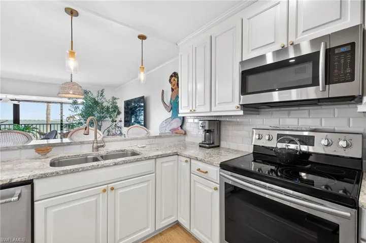 Kitchen featuring white cabinetry, light-toned granite countertops, a stainless steel double basin sink with a gooseneck faucet, a subway tile backsplash, and stainless steel appliances