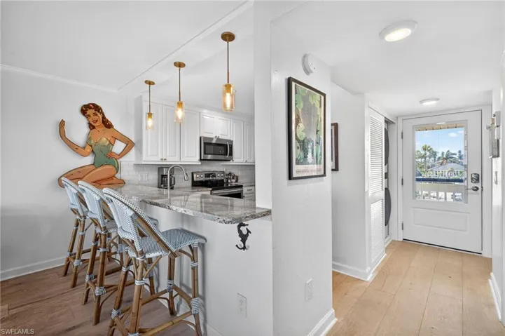 Kitchen featuring a breakfast bar with pendant lighting, white shaker cabinetry, stainless steel appliances, and a tile backsplash