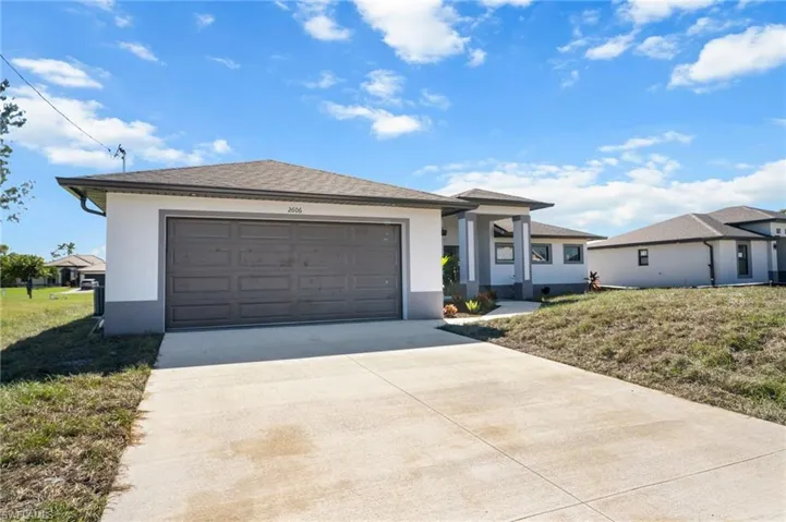 View of front of property featuring stucco siding, concrete driveway, a front lawn, and an attached garage