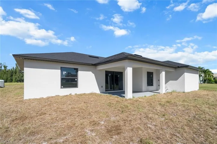 Back of property featuring a lawn, stucco siding, and a patio area